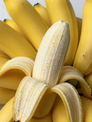 Šviežias bananas, sveikas ir pjaustytas, dubenyje ir ant kaimiško stalo